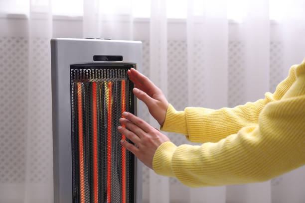 Woman warming hands near infrared heater indoors,